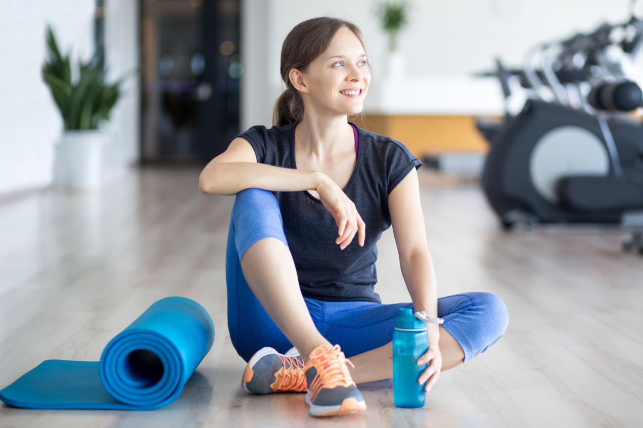 Happy sporty woman on floor with mat and water